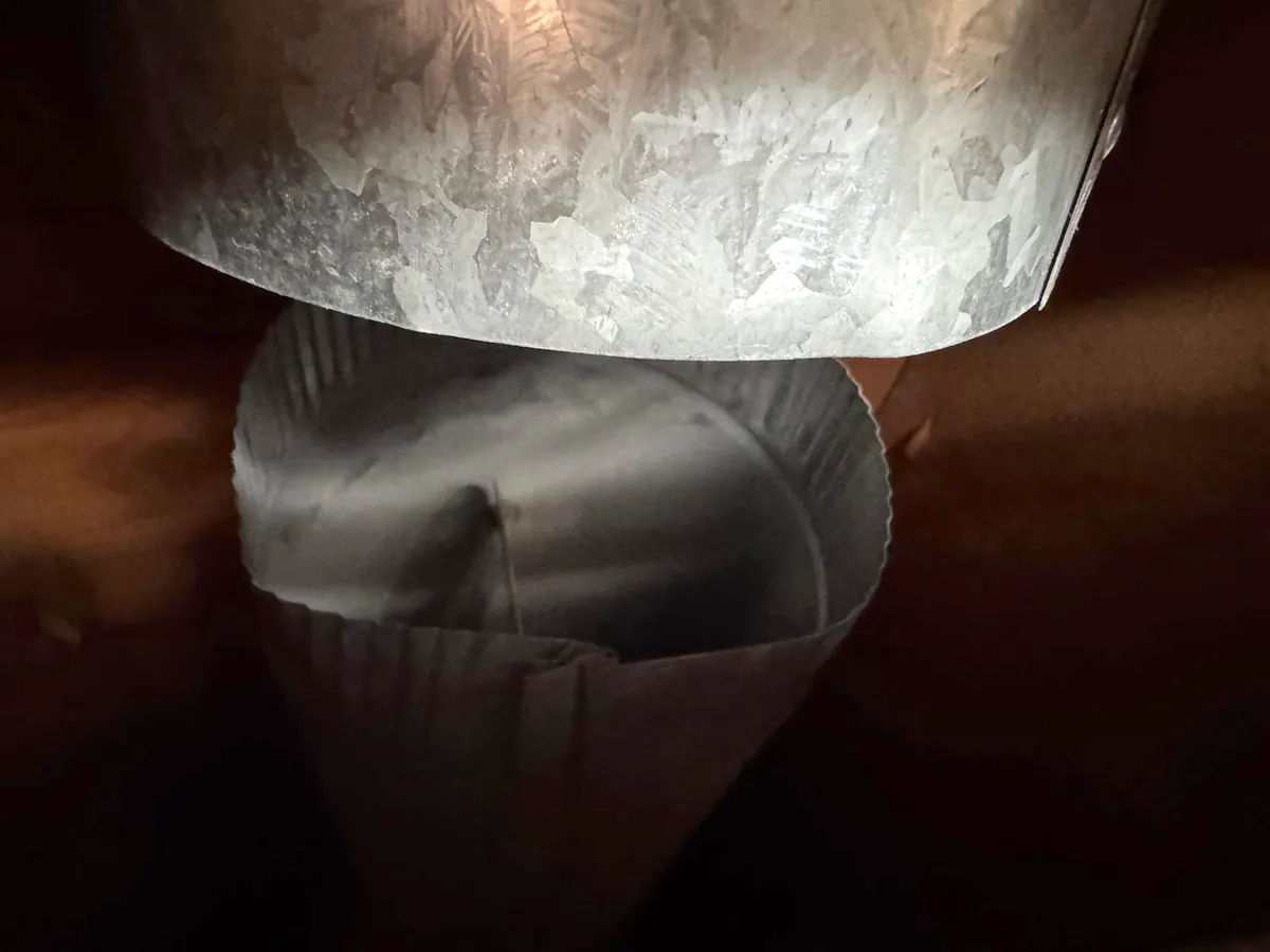 Close-up in low light of a round galvanized duct pulled apart from the crimped end it's meant to fit over, leaving the duct open