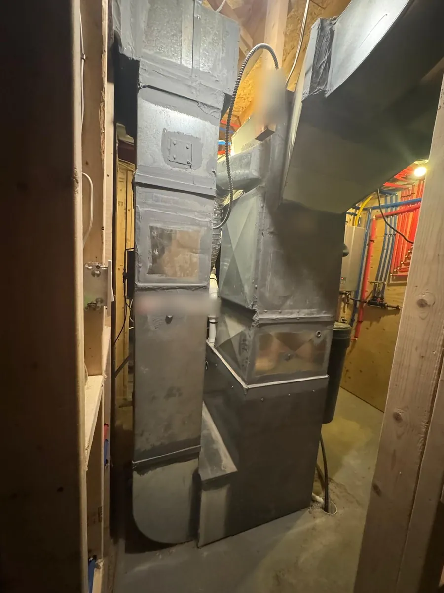 Furnace and sheet-metal plenum and ductwork in an unfinished basement mechanical room, with red and blue PEX plumbing lines in the background