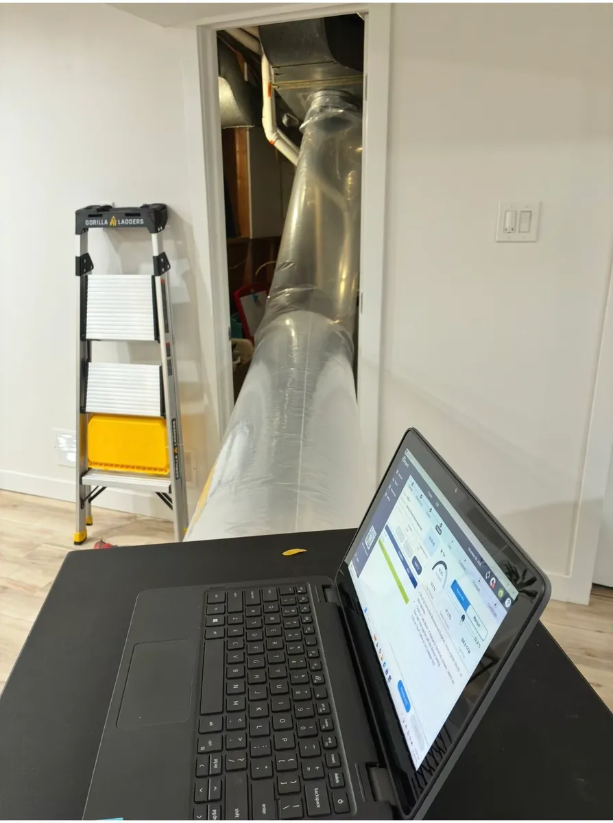 Clear Aeroseal injection tube running across a finished basement into the mechanical room, with a laptop running the Aeroseal software in the foreground