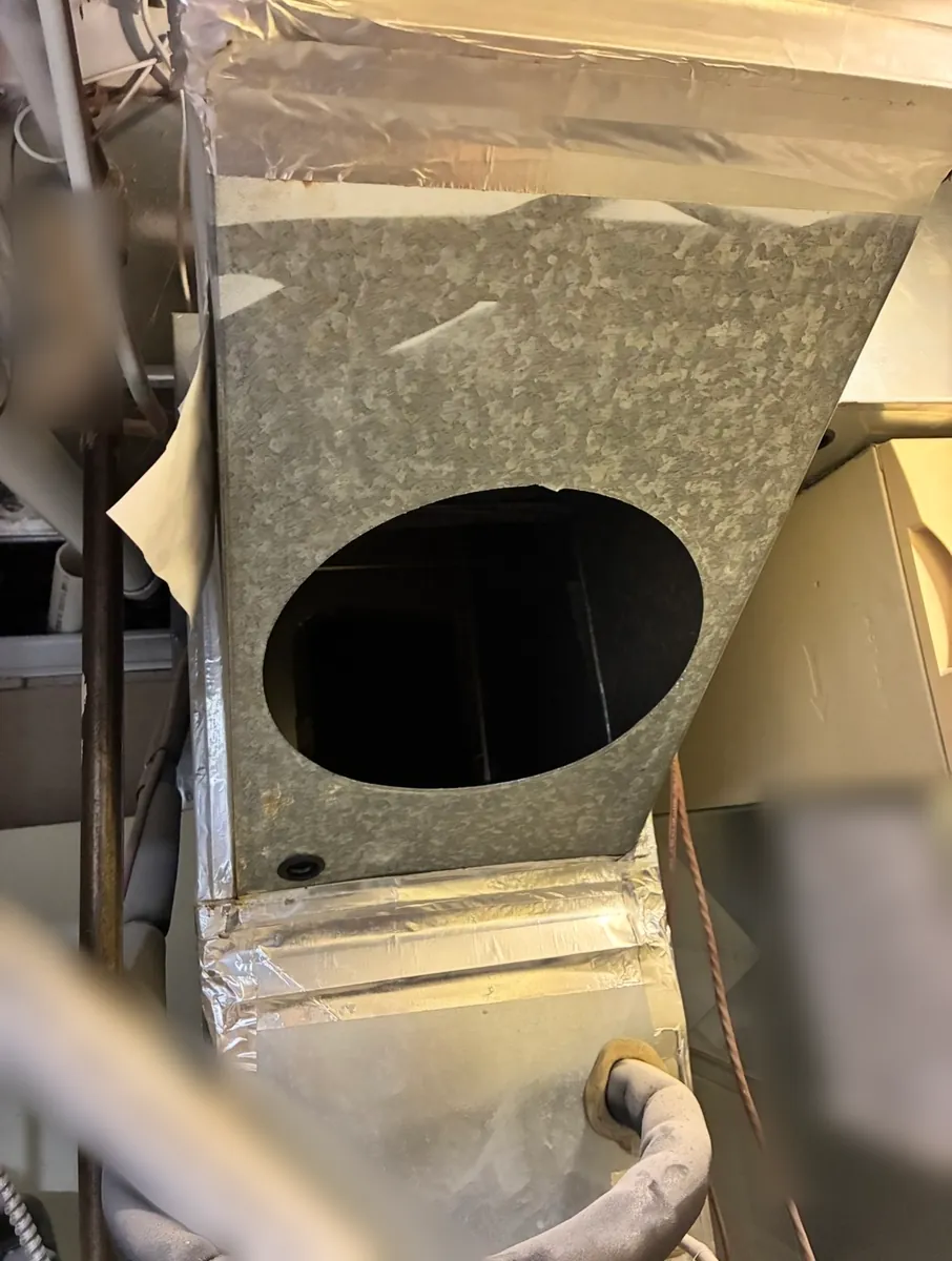 Galvanized supply plenum above a furnace with a large round opening in its side and foil tape on the seams
