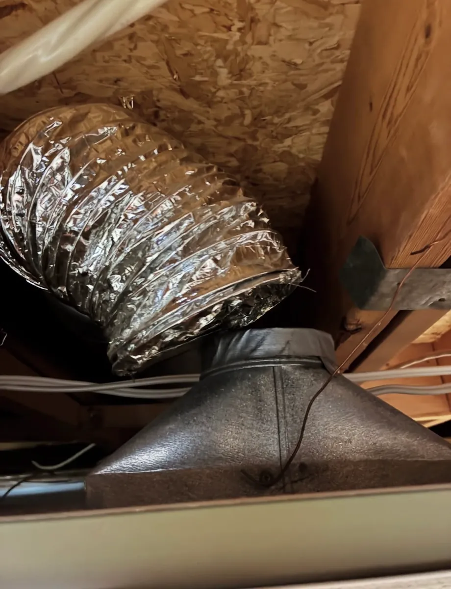 Looking up into an open ceiling at a foil flex duct sitting off the metal register boot it should connect to