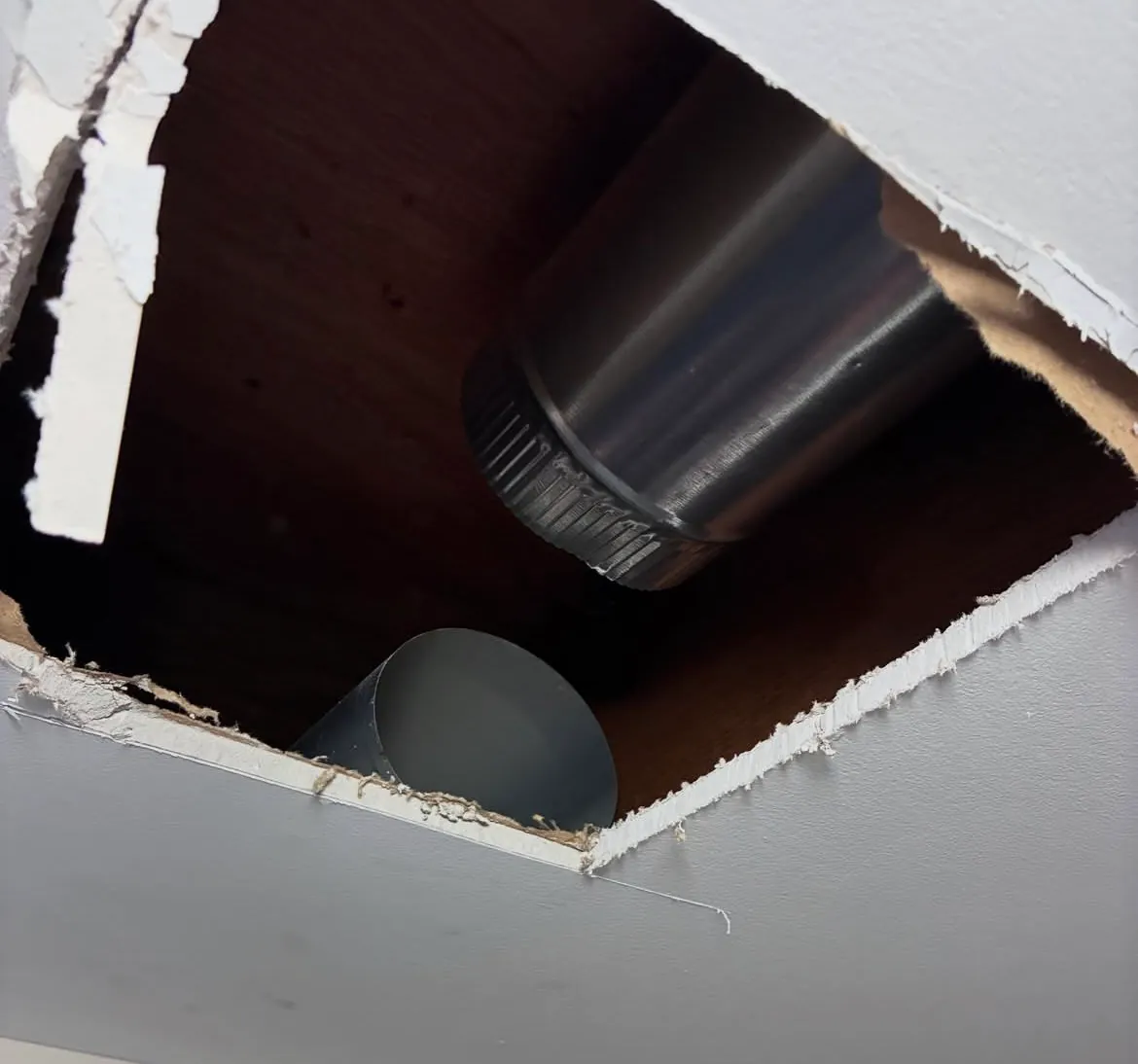 Opening in a basement drywall ceiling with two round metal duct ends hanging apart inside, no longer connected to each other